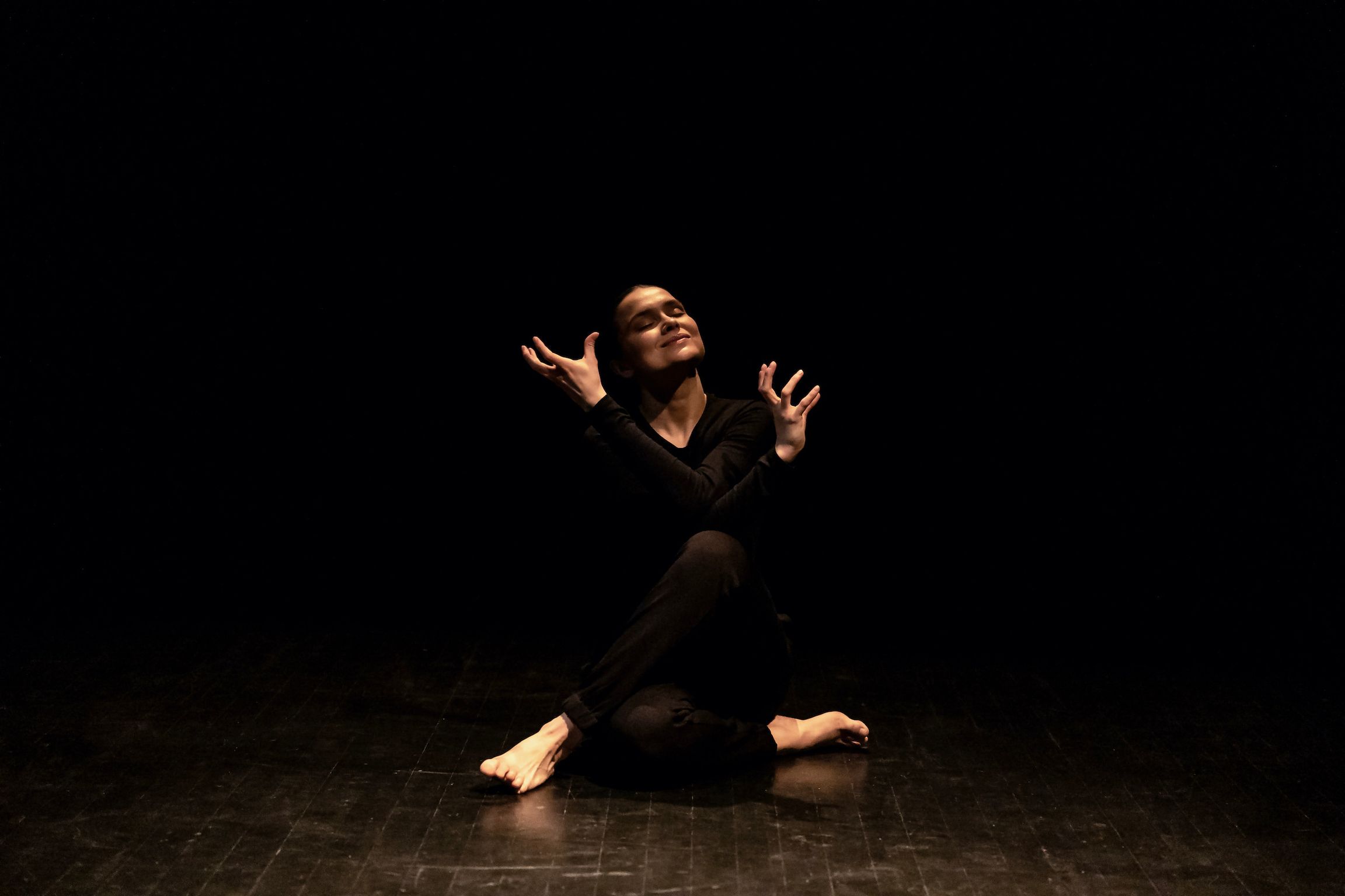 Anetta sitting smiling with her eyes closed, her legs and arms crossed, palms open.