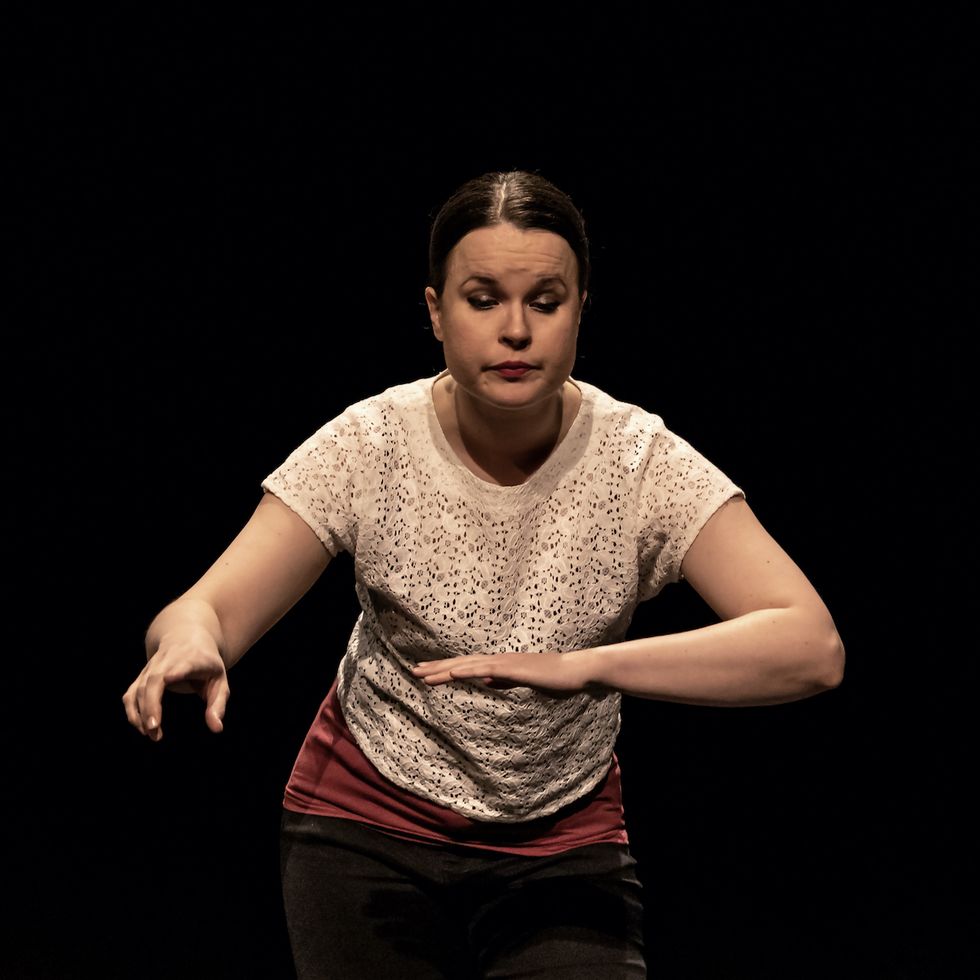Kati on stage, slightly bent against an invisible work desk, with an invisible mouse in her hand