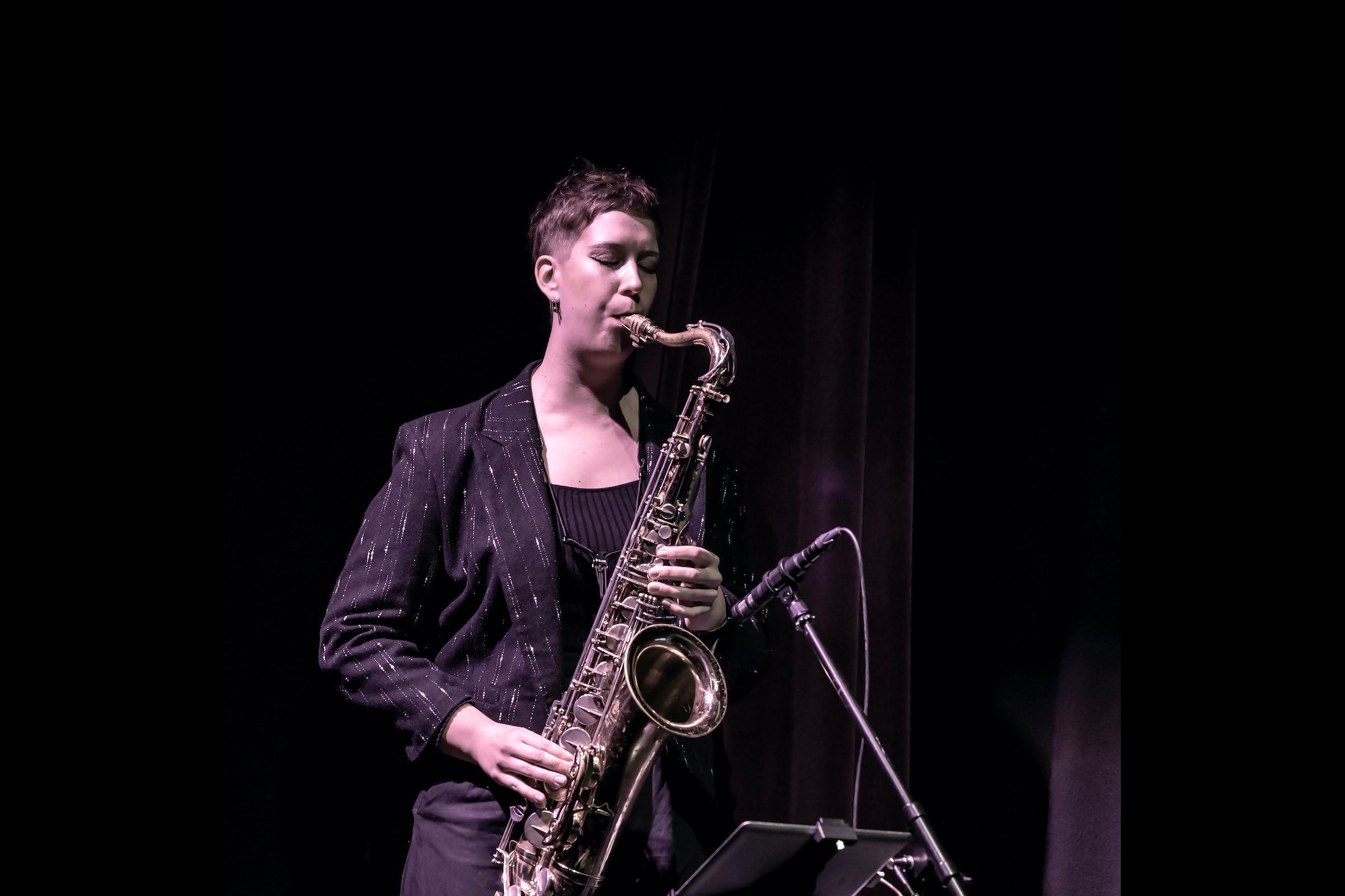 Heli playing the saxophone on stage with her eyes closed.