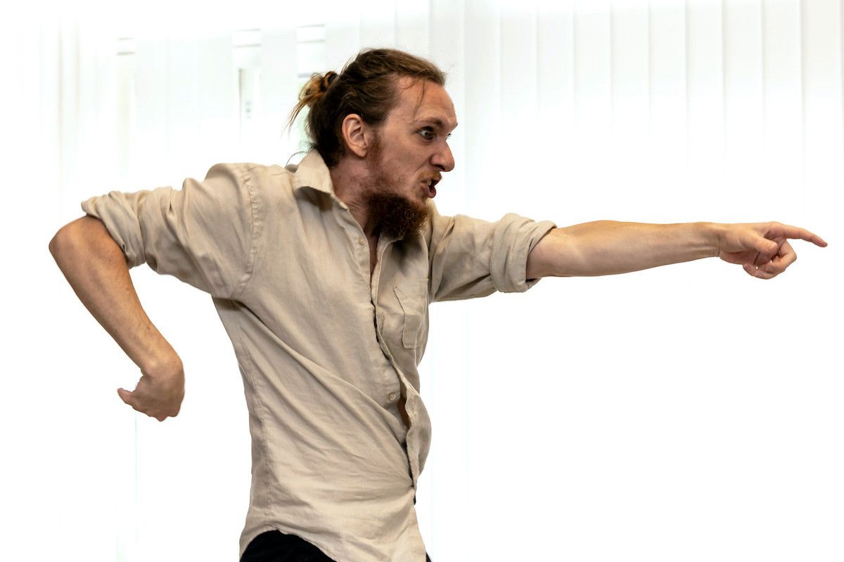 Crazy-looking Tomaš pointing forward with his left arm, the right arm bent behind his back