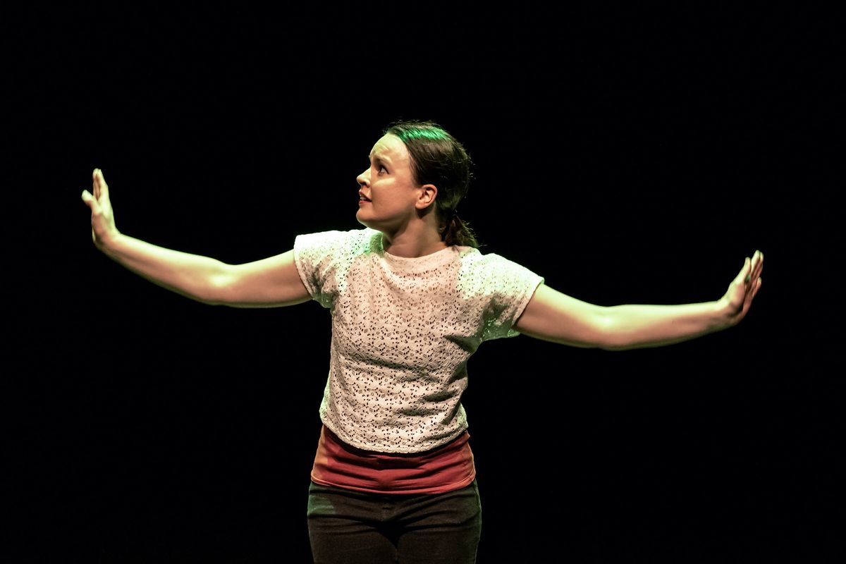 Kati on stage, looking worried at her side, with her arms spread like wings