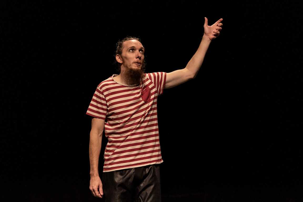 Tomaš on stage in little boy’s clothes, looking up and holding his invisible mother’s hand.